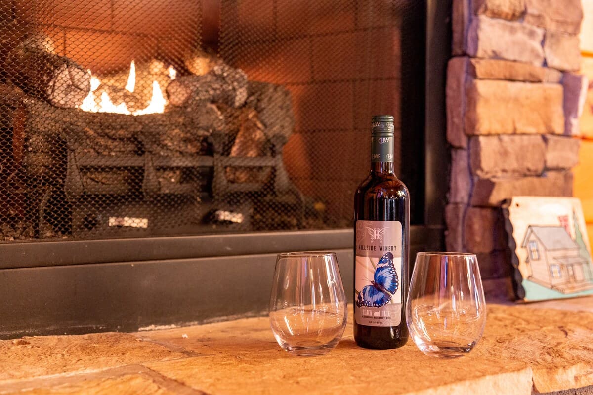 Hillside Winery wine bottle and two stemless glasses on stone fireplace hearth with fire burning
