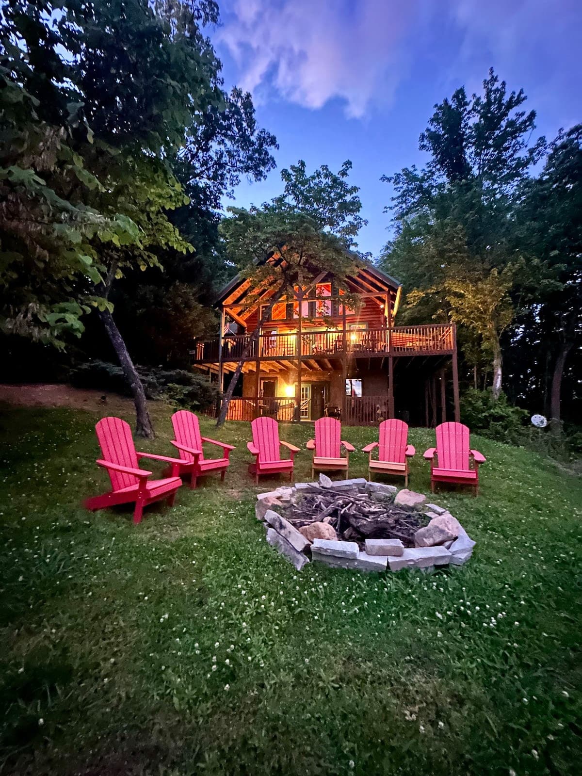 Thistle Britches cabin glowing warmly at night, two-story A-frame with wraparound decks surrounded by dark trees