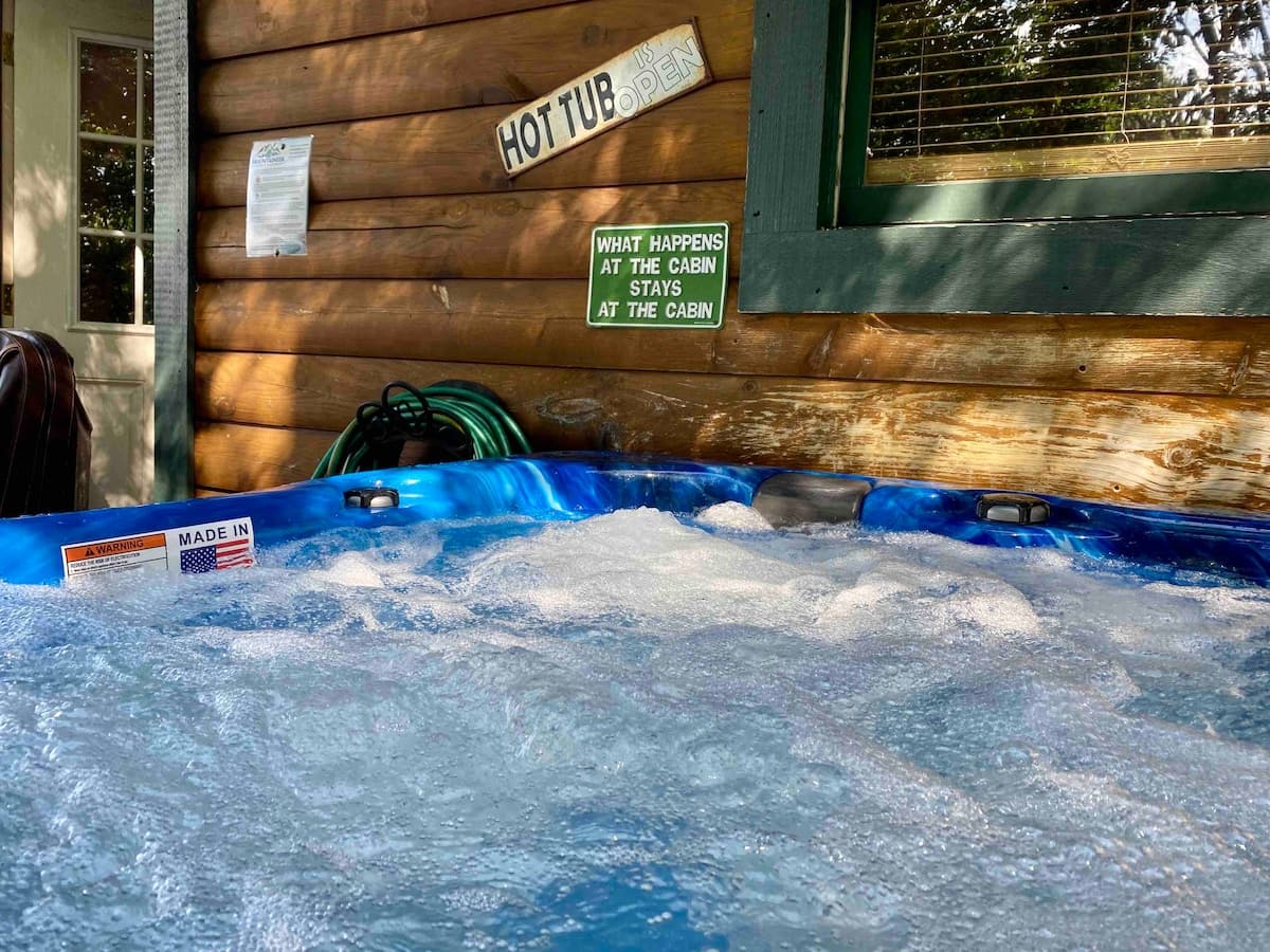 Hot tub bubbling on the deck with fun cabin signs and lush forest backdrop