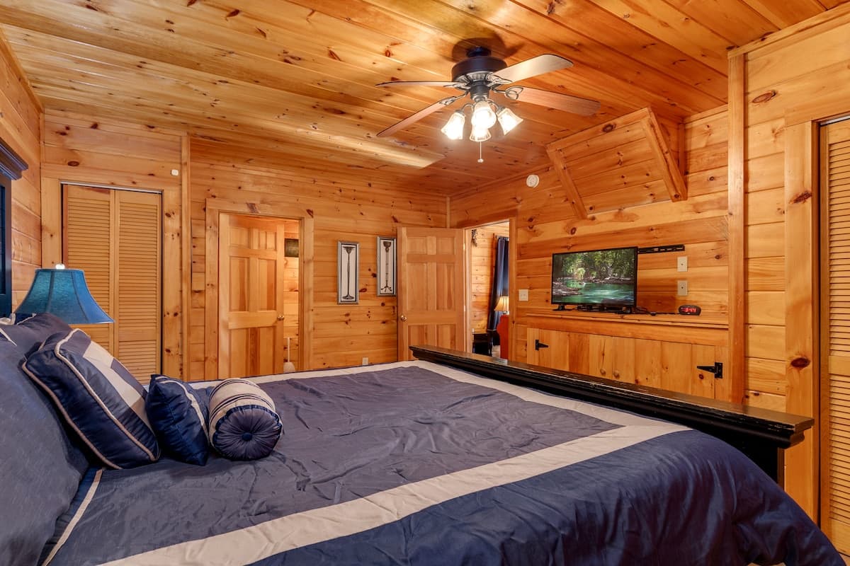Bedroom with navy blue bedding, mounted TV, and pine ceiling