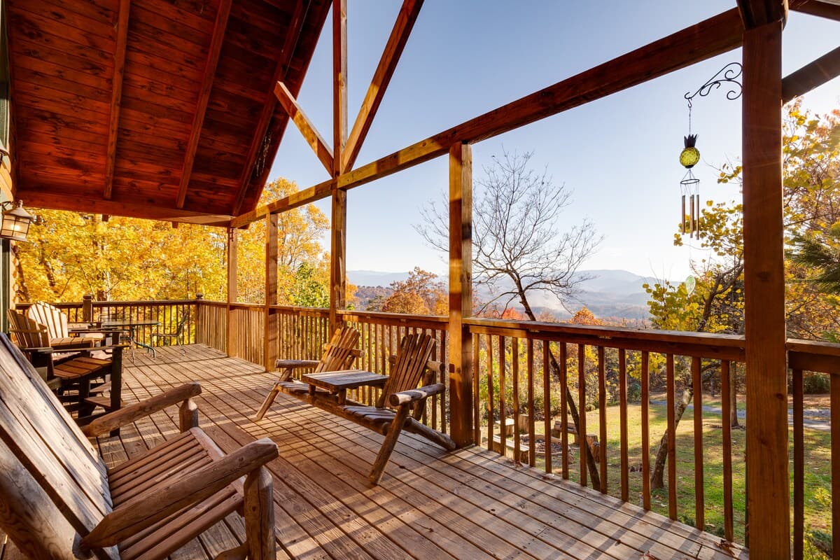 Covered upper deck with rocking chairs, wind chimes, and mountain views through autumn trees