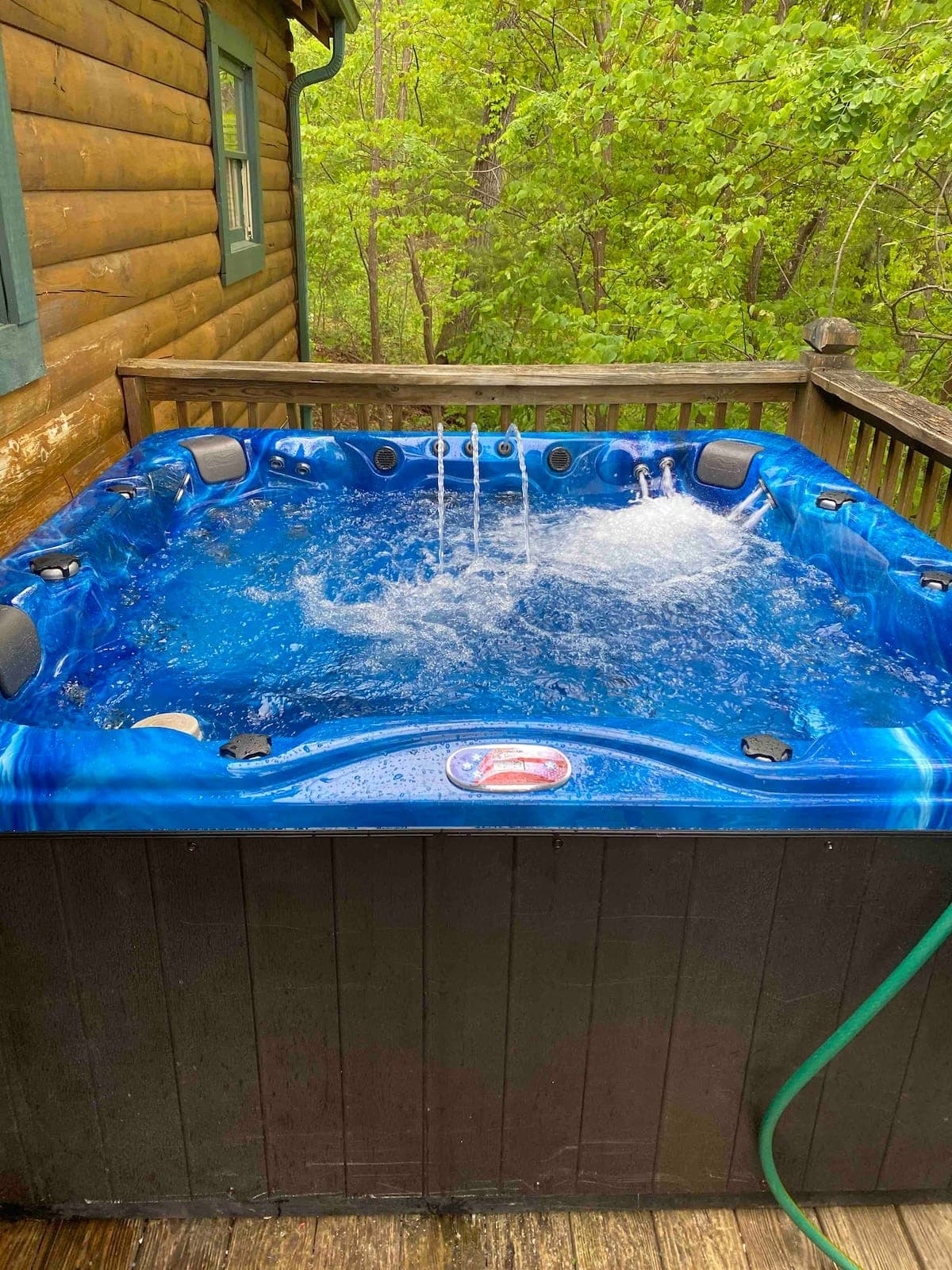 Blue 7-person premium hot tub with jets and LED waterfall running on the cabin deck