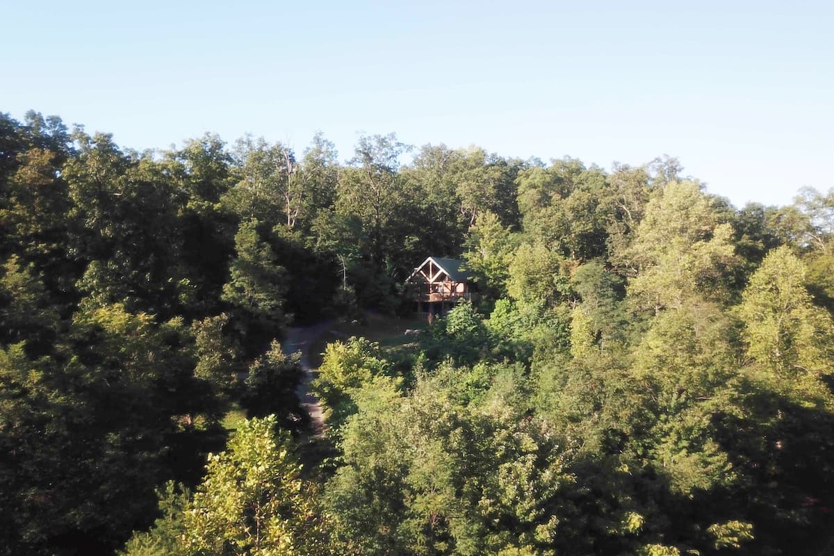 Drone view showing the cabin hidden among dense forest at the highest point on the mountain