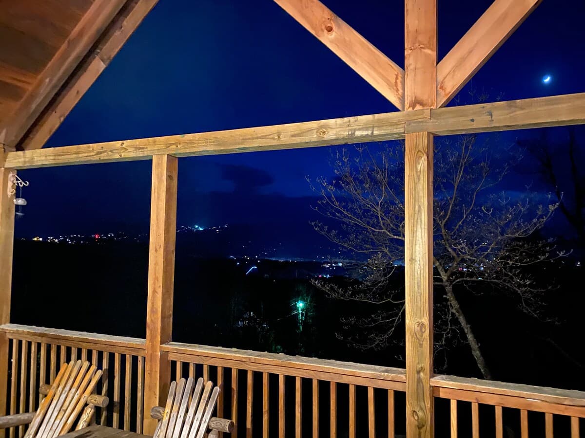 Night view from covered upper deck with rocking chairs, city lights twinkling through timber A-frame beams